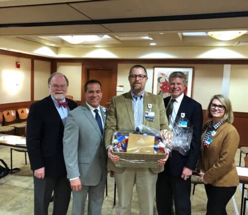 Five healthcare professionals in business attire presenting a gift basket in conference room