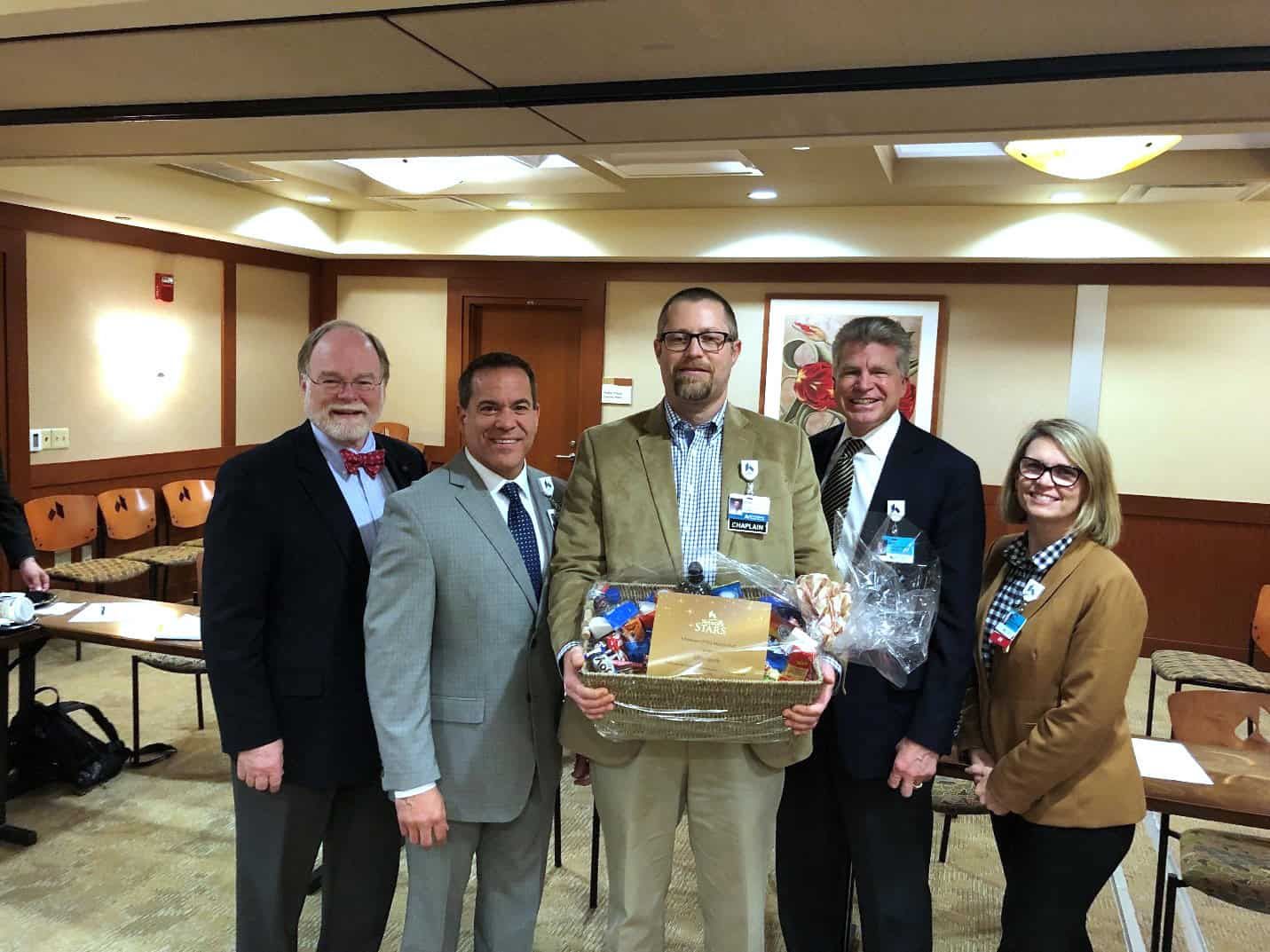 Five healthcare professionals in business attire presenting a gift basket in conference room