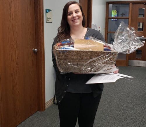 Woman holding large wrapped gift basket in office hallway