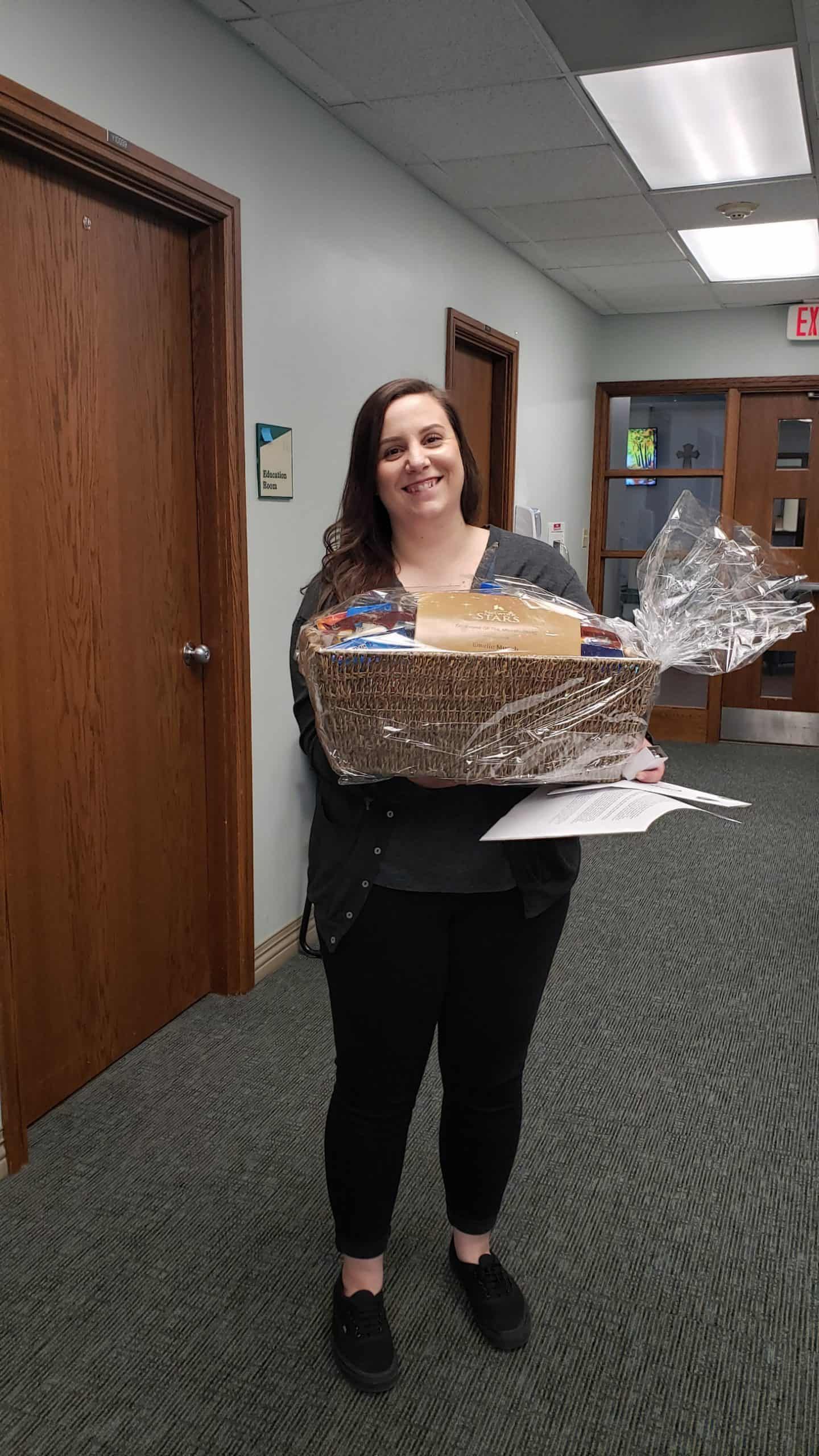 Woman holding large wrapped gift basket in office hallway