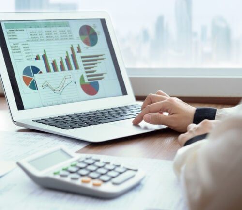 Person analyzing financial charts and graphs on laptop with calculator nearby