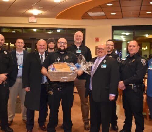 Group of police officers and hospital staff presenting gift basket to colleague
