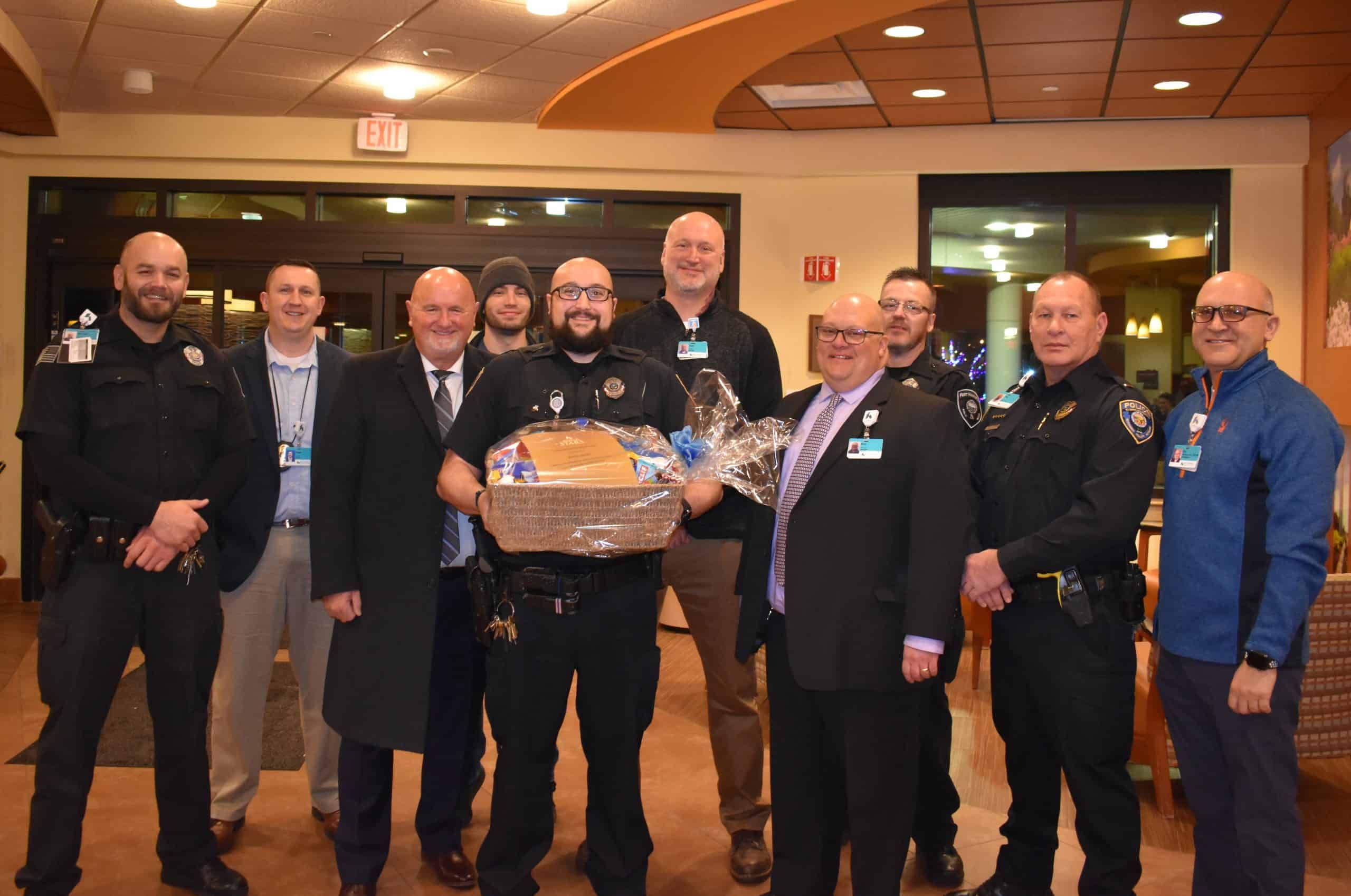 Group of police officers and hospital staff presenting gift basket to colleague