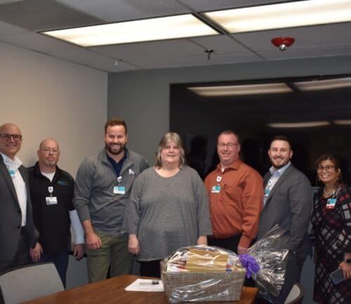 Group of healthcare professionals posing with employee recognition gift basket in conference room