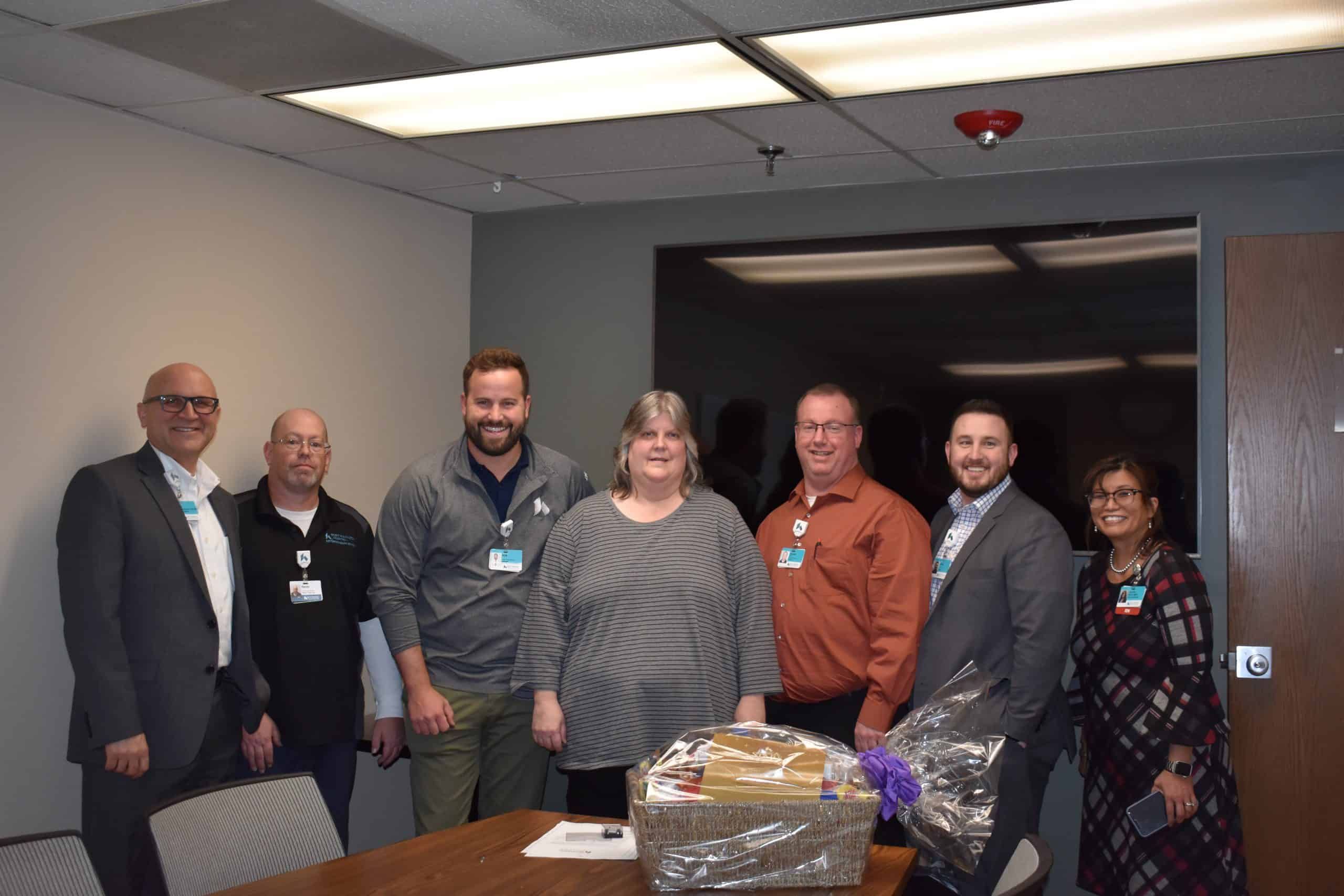 Group of healthcare professionals posing with employee recognition gift basket in conference room