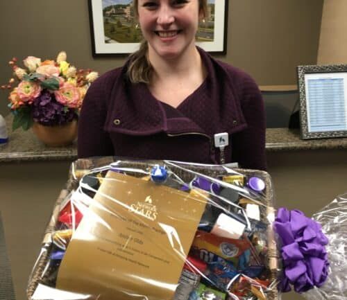 Healthcare employee holding gift basket with certificate and purple ribbon at reception desk