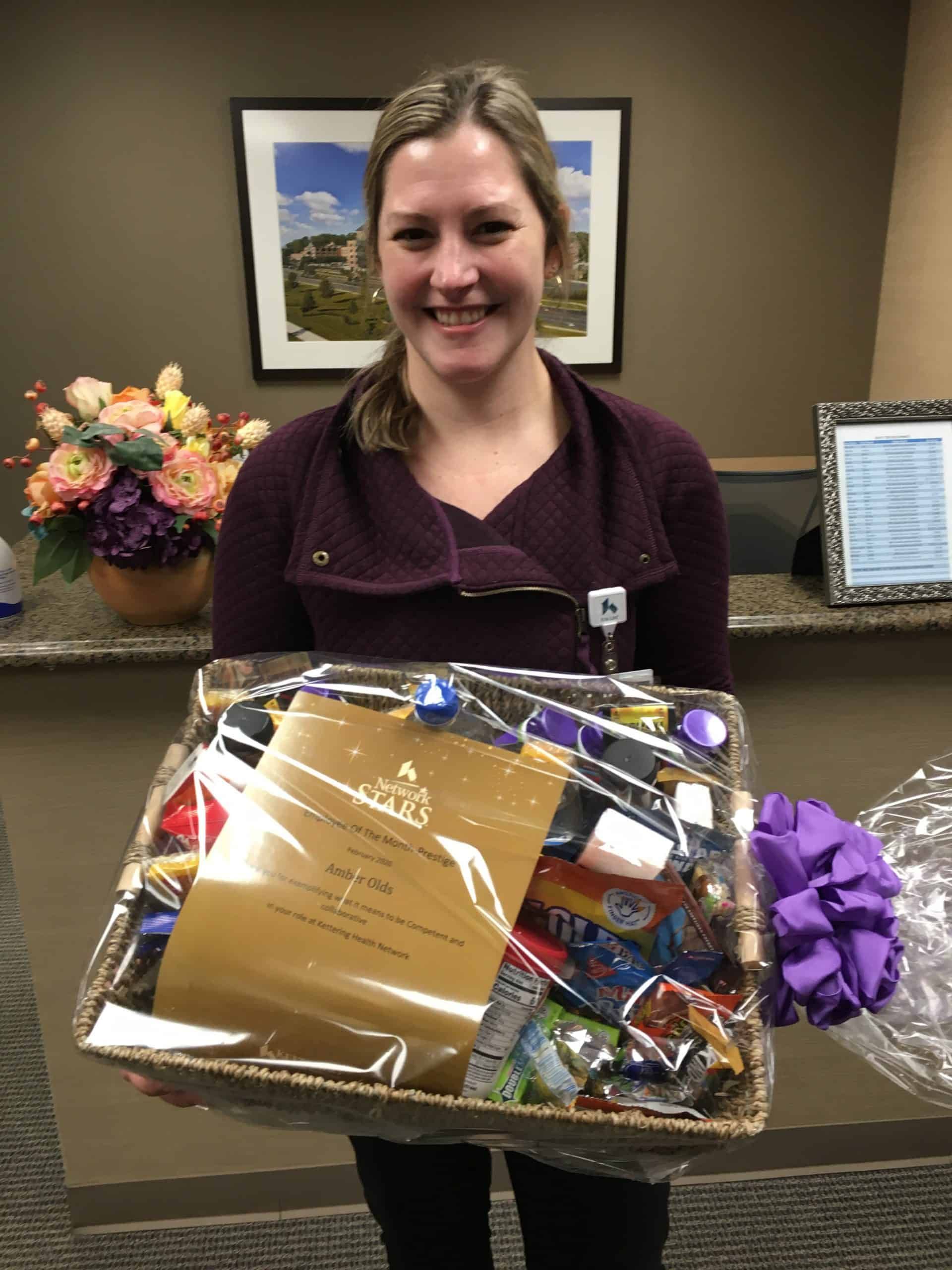 Healthcare employee holding gift basket with certificate and purple ribbon at reception desk