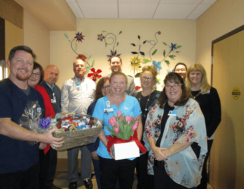 Healthcare staff celebrating employee of the month Angela Church with gift basket and flowers.