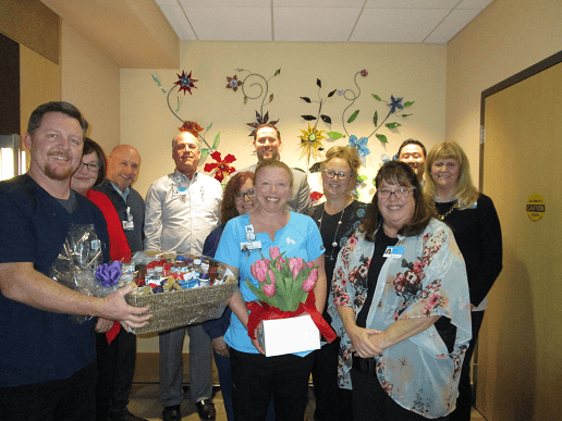 Healthcare staff celebrating employee of the month Angela Church with gift basket and flowers.