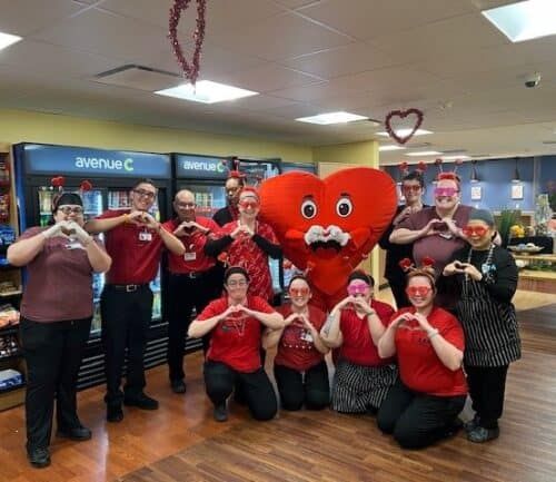 Healthcare staff in red clothing making heart gestures with hands around large heart mascot