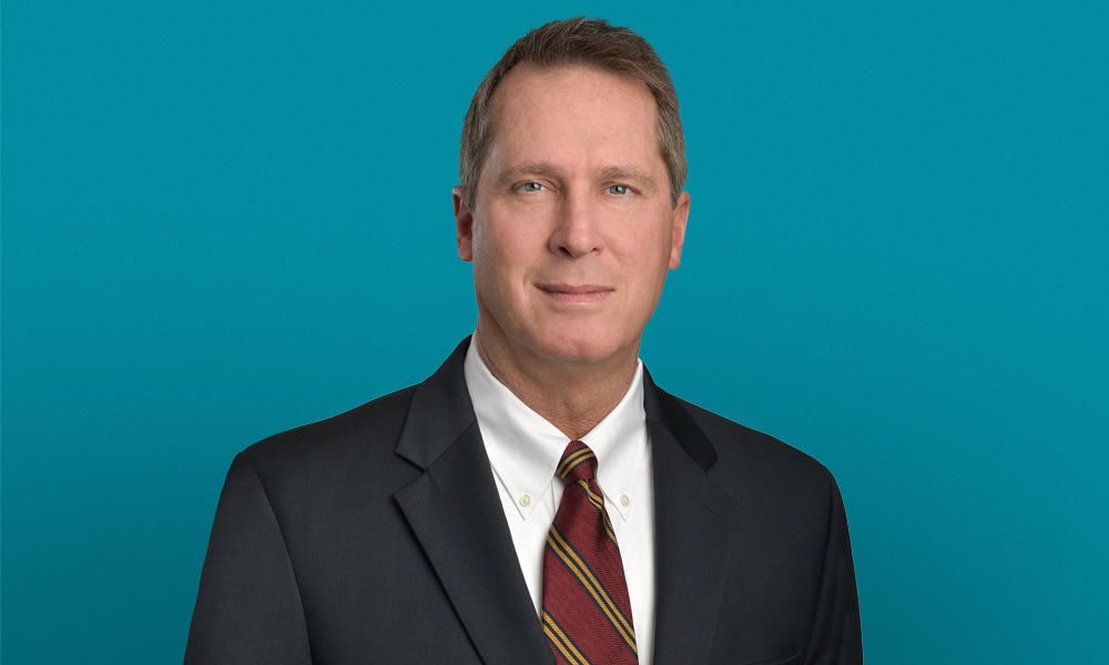 Professional headshot of Mike Gentry in dark suit against teal background