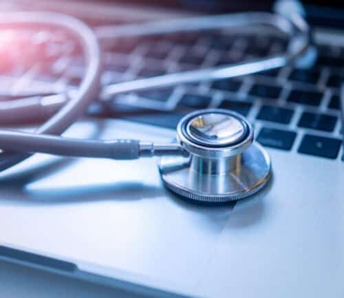 Stethoscope resting on laptop keyboard next to pen, representing digital healthcare technology.