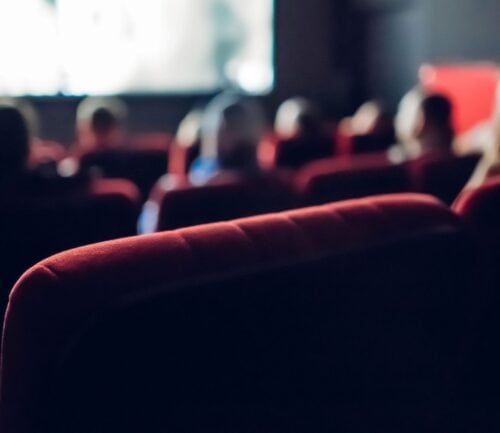 People sitting in red theater seats watching a presentation or movie screen.