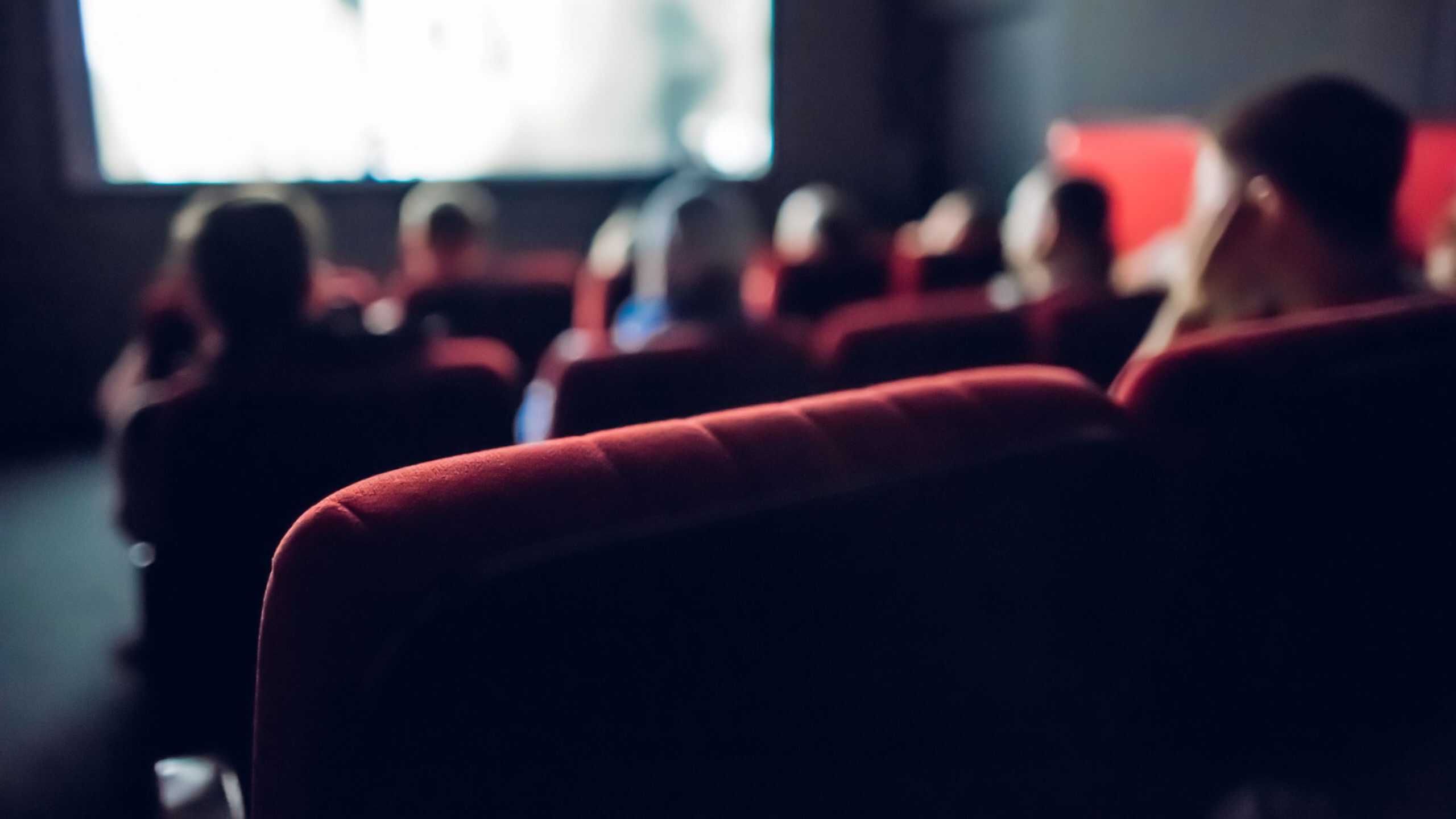 People sitting in red theater seats watching a presentation or movie screen.