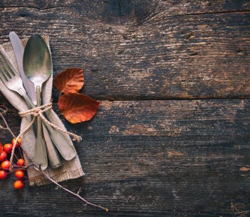 Vintage silverware tied with burlap ribbon and autumn berries on weathered wooden table
