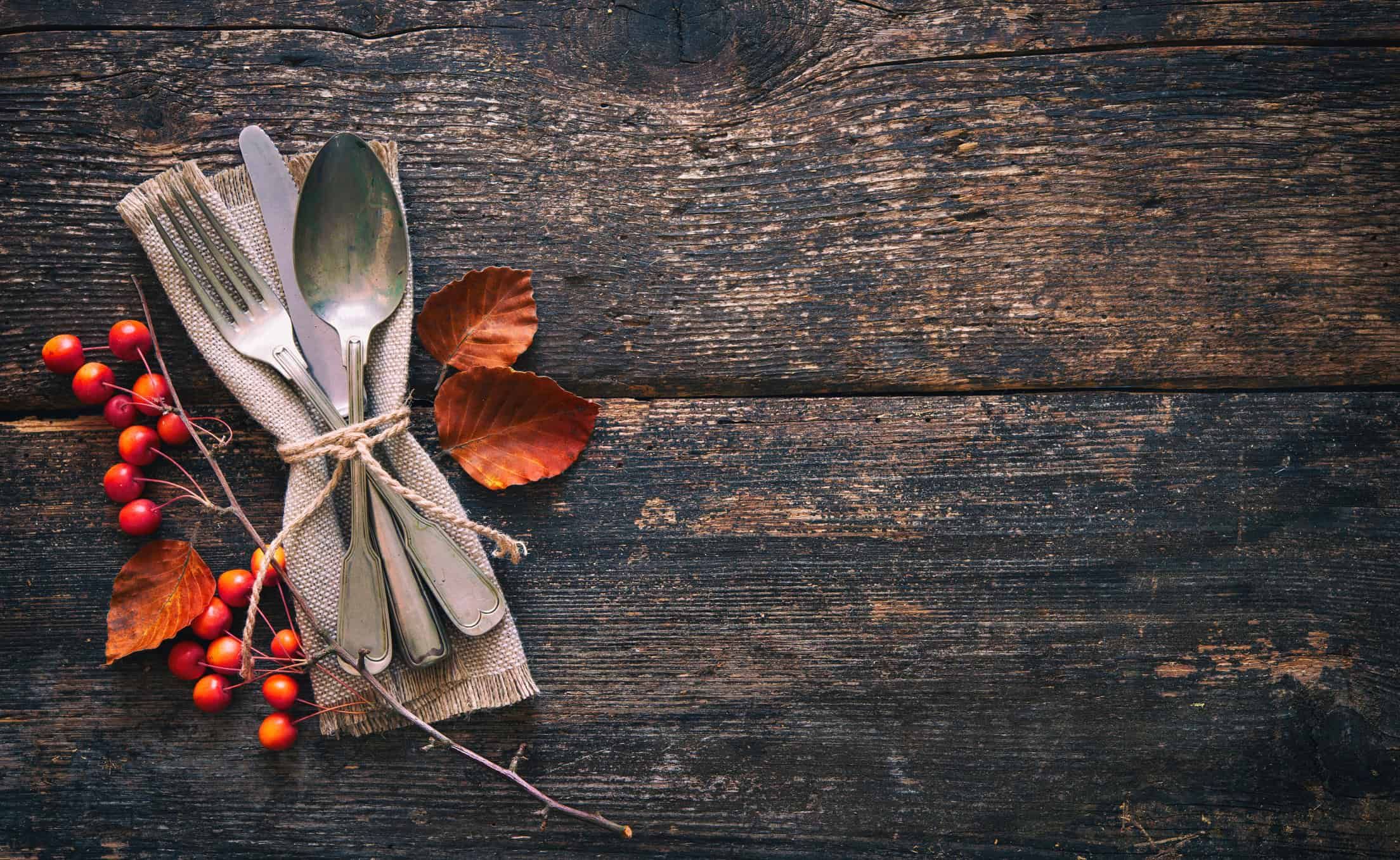 Vintage silverware tied with burlap ribbon and autumn berries on weathered wooden table