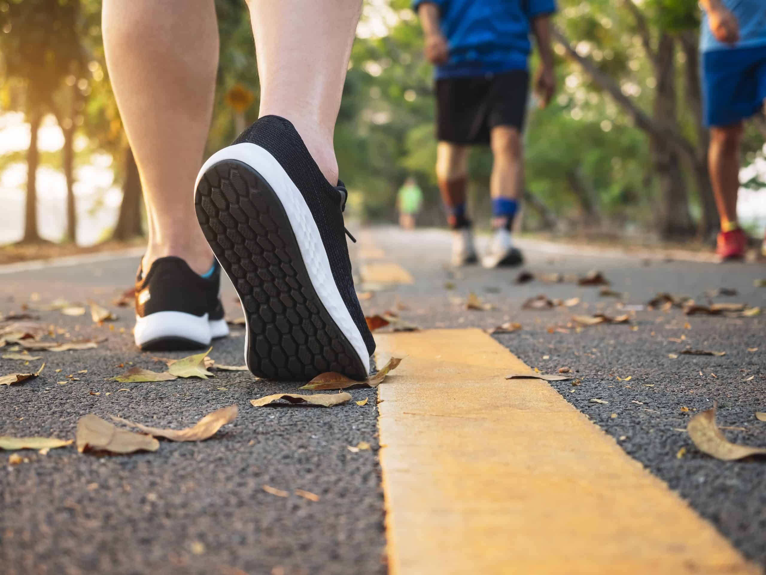 Runner's feet in black sneakers on yellow-lined asphalt path with fallen leaves