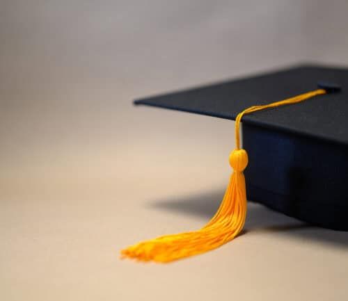 Black graduation cap with gold tassel on neutral background