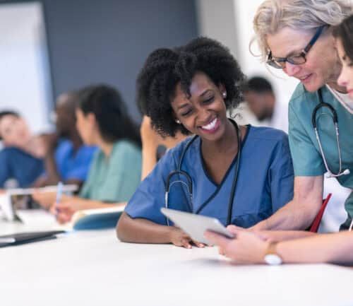 Senior female medical instructor teaching diverse students with stethoscopes using tablet