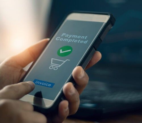 Hand holding smartphone displaying "Payment Completed" confirmation with green checkmark and shopping cart icon