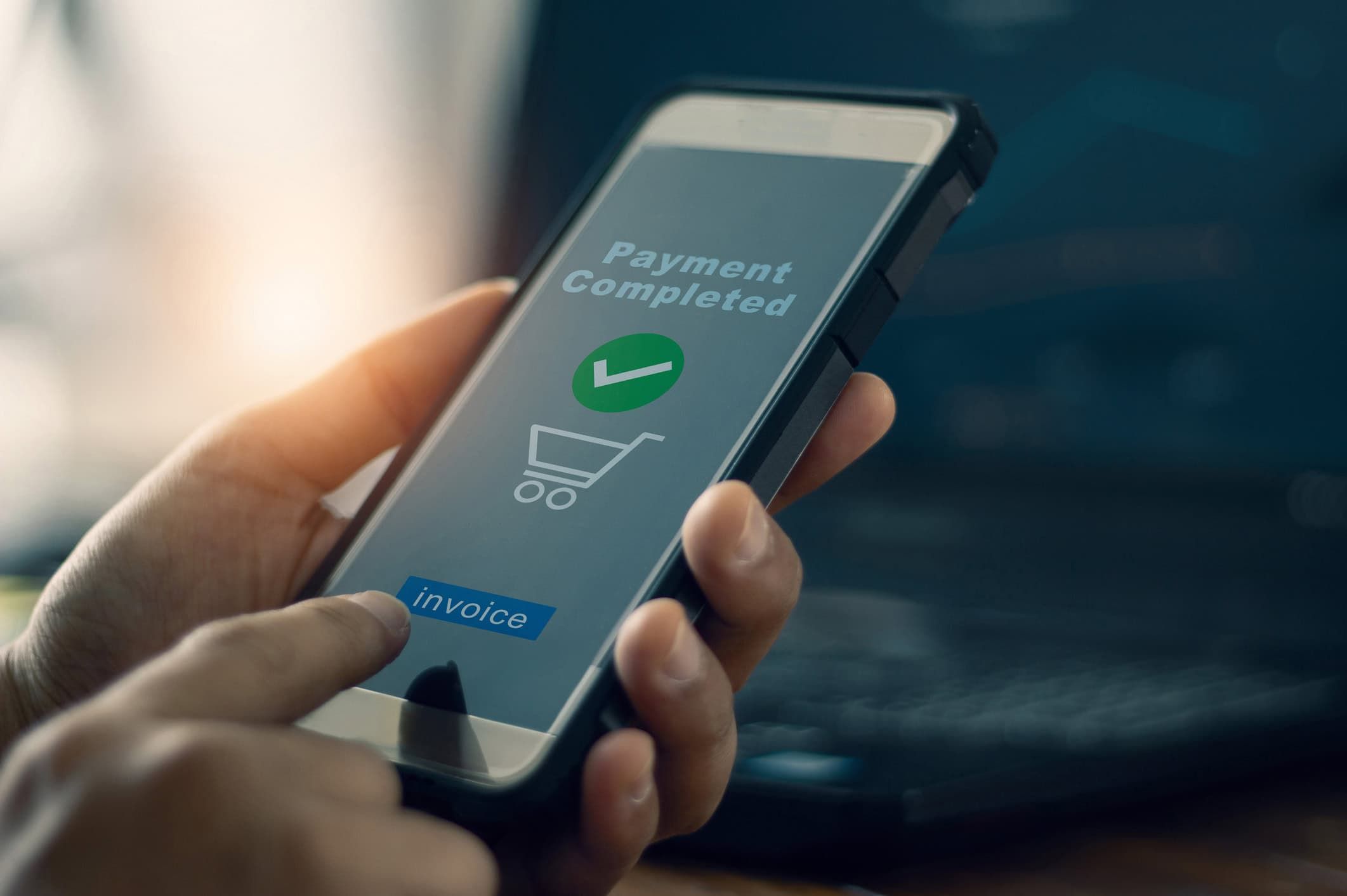 Hand holding smartphone displaying "Payment Completed" confirmation with green checkmark and shopping cart icon