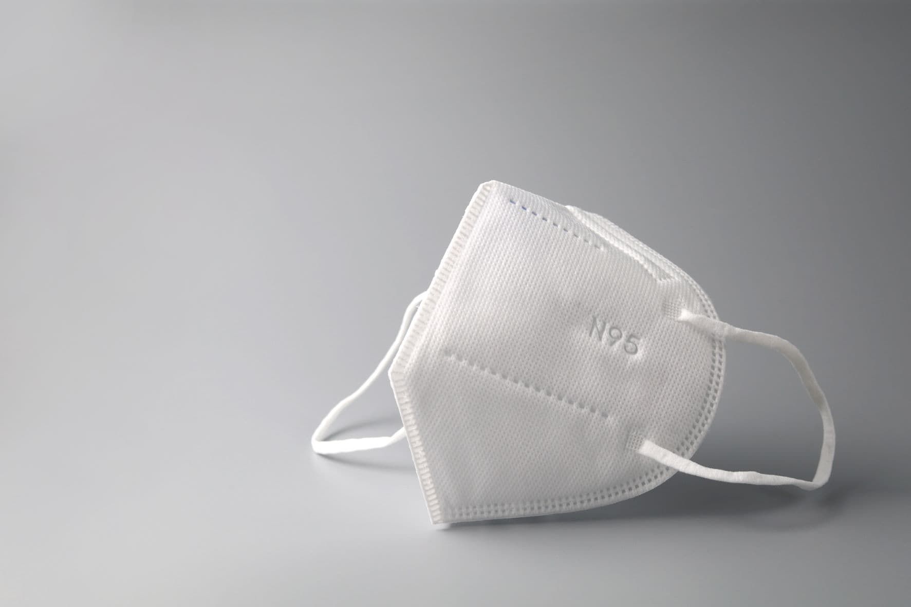 White N95 respirator mask with ear straps on gray background