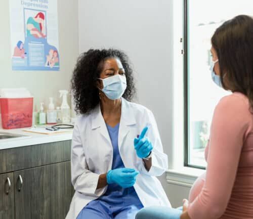 Doctor in mask gestures while consulting with pregnant patient in medical office
