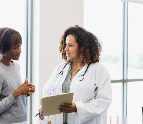 Female doctor with stethoscope discussing medical records with senior woman patient