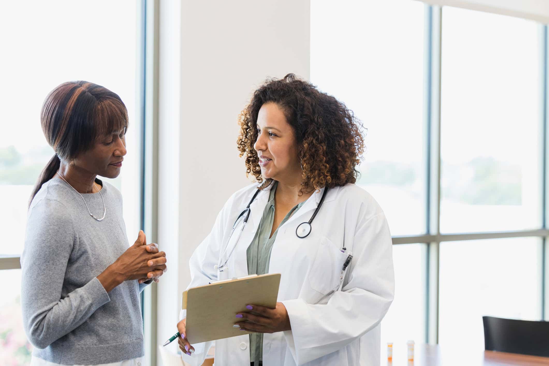 Female doctor with stethoscope discussing medical records with senior woman patient