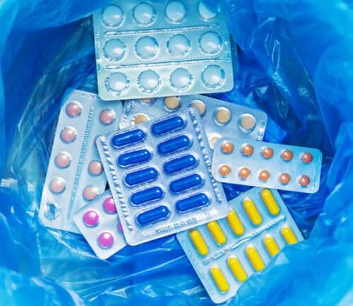 Various medication blister packs and pills discarded in blue plastic trash bag.