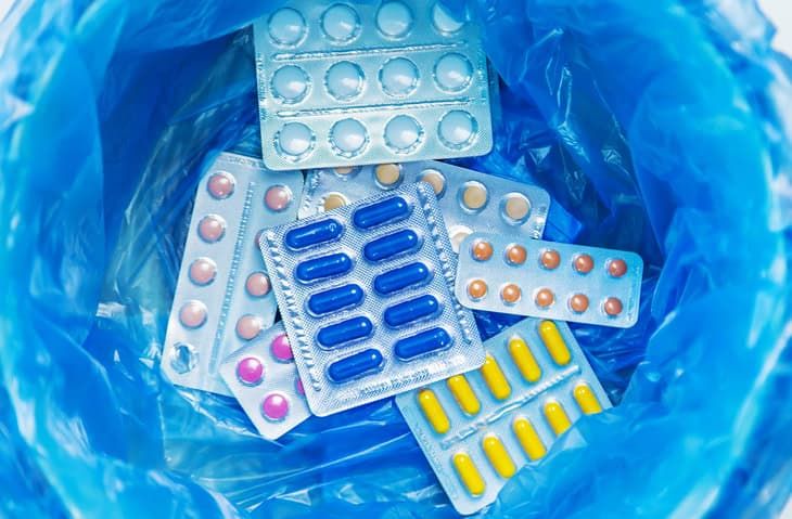 Various medication blister packs and pills discarded in blue plastic trash bag.