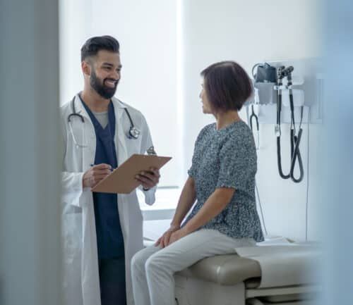Doctor with stethoscope consulting female patient sitting on examination table in medical office