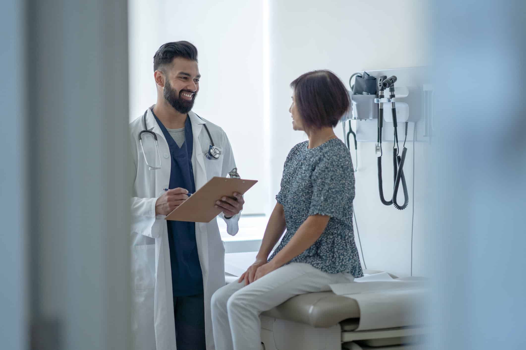 Doctor with stethoscope consulting female patient sitting on examination table in medical office