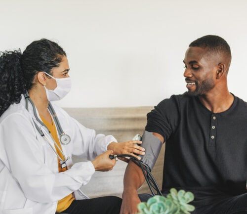 Doctor wearing mask takes blood pressure of smiling man during home visit