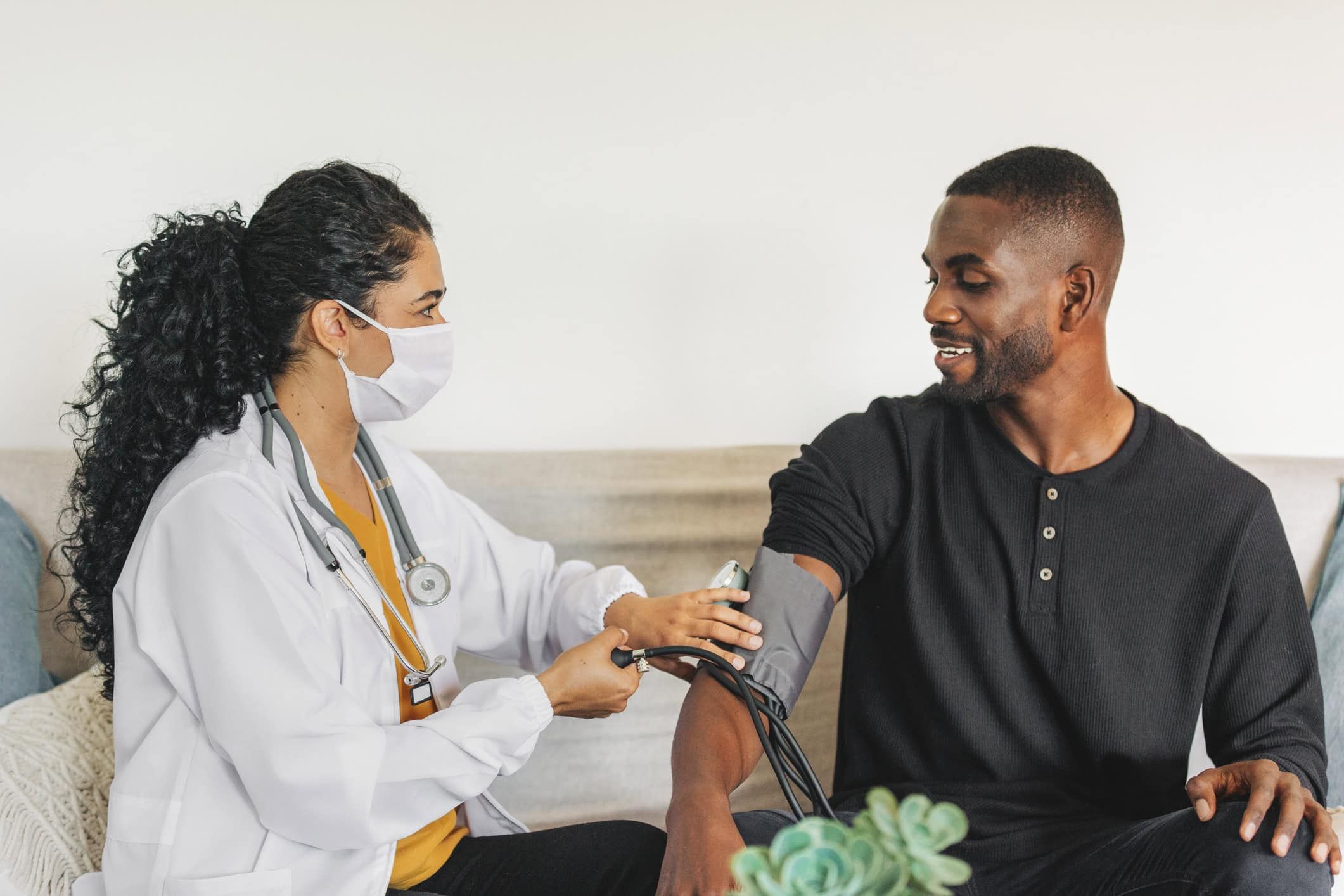 Doctor wearing mask takes blood pressure of smiling man during home visit