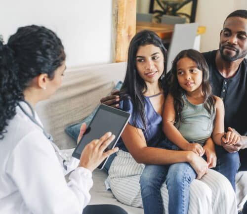 Healthcare provider with tablet consulting with family of three on couch