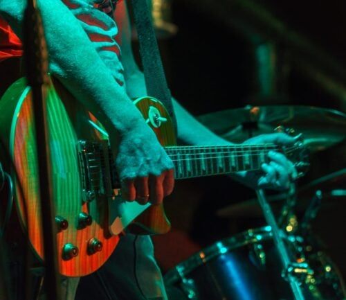 Musician playing electric guitar on stage with colorful green and red lighting