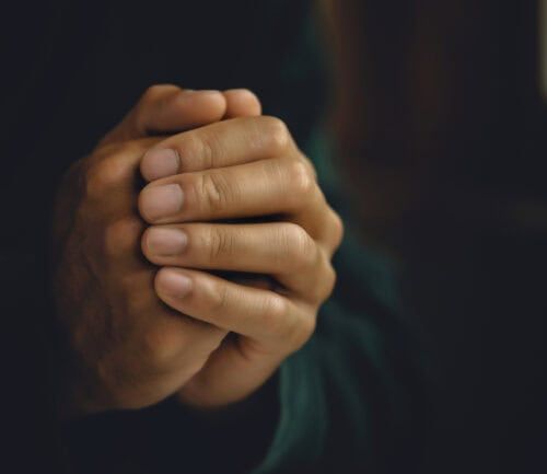 Clasped hands in prayer position against blurred dark background