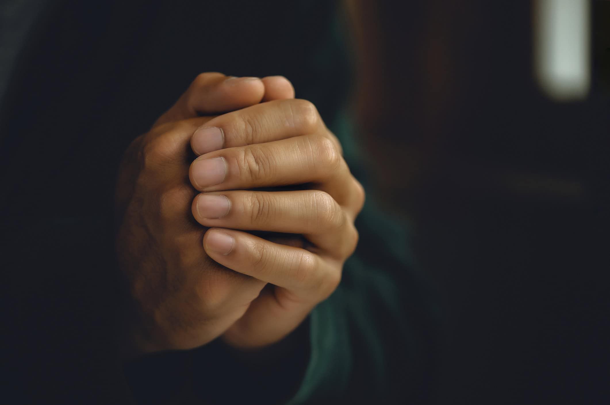Clasped hands in prayer position against blurred dark background