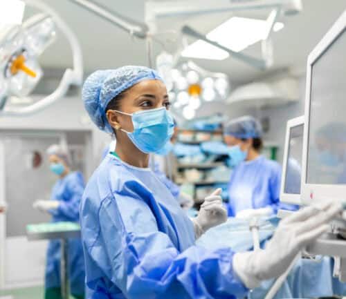 Anesthetist in blue scrubs and mask monitoring equipment in hospital operating room