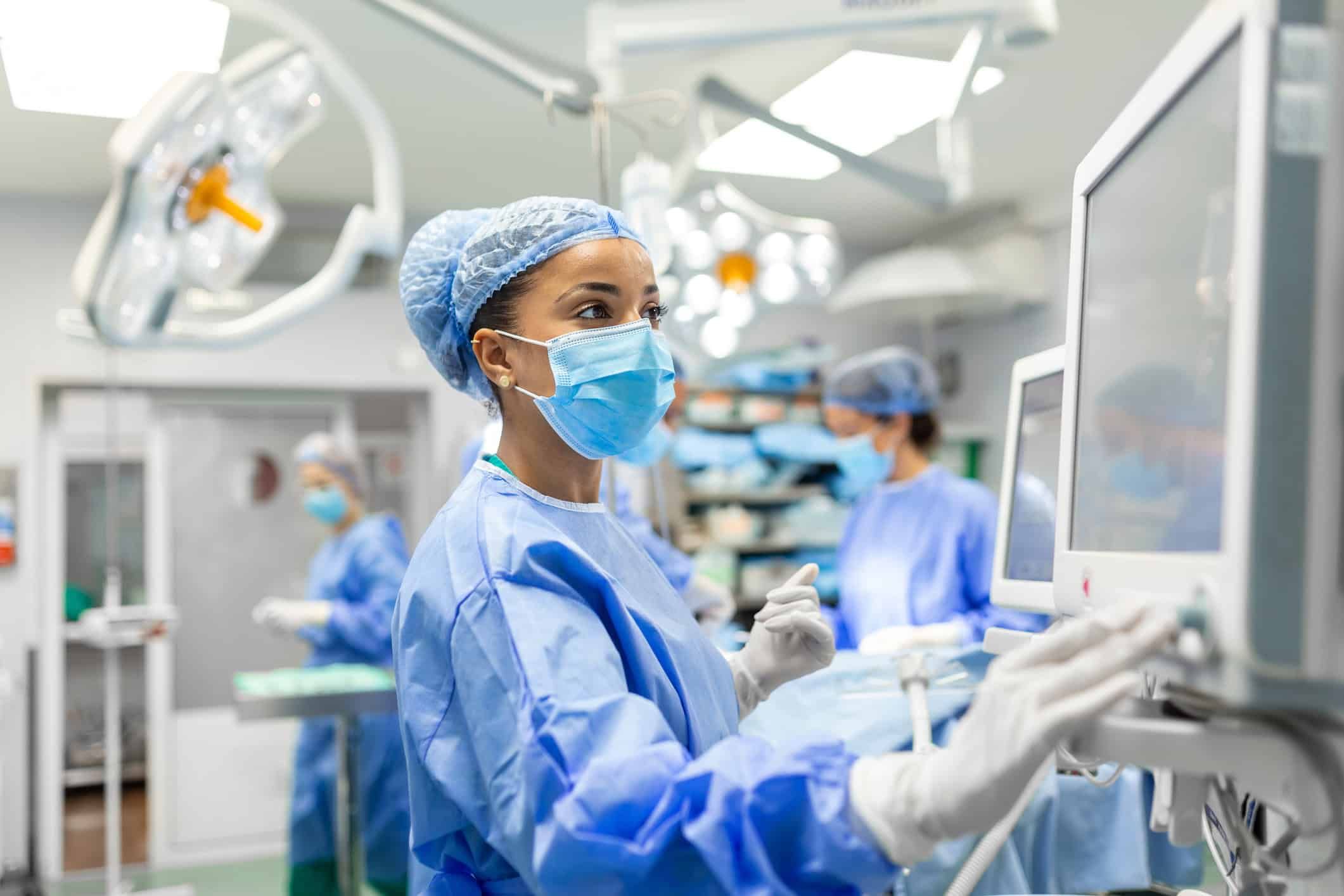 Anesthetist in blue scrubs and mask monitoring equipment in hospital operating room