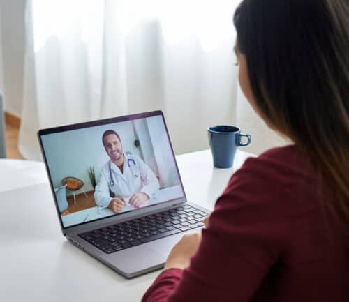 Woman having virtual therapy session with doctor on laptop at home