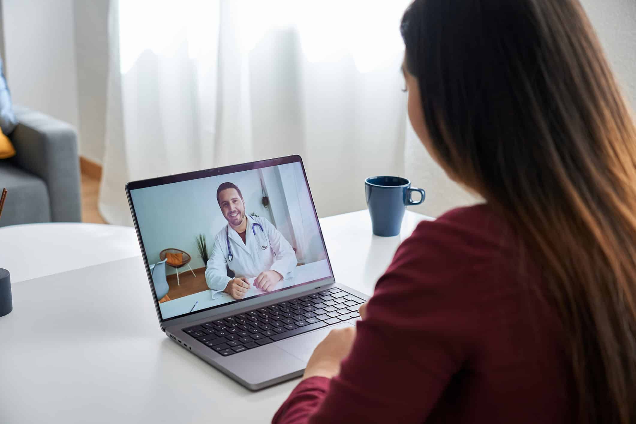 Woman having virtual therapy session with doctor on laptop at home