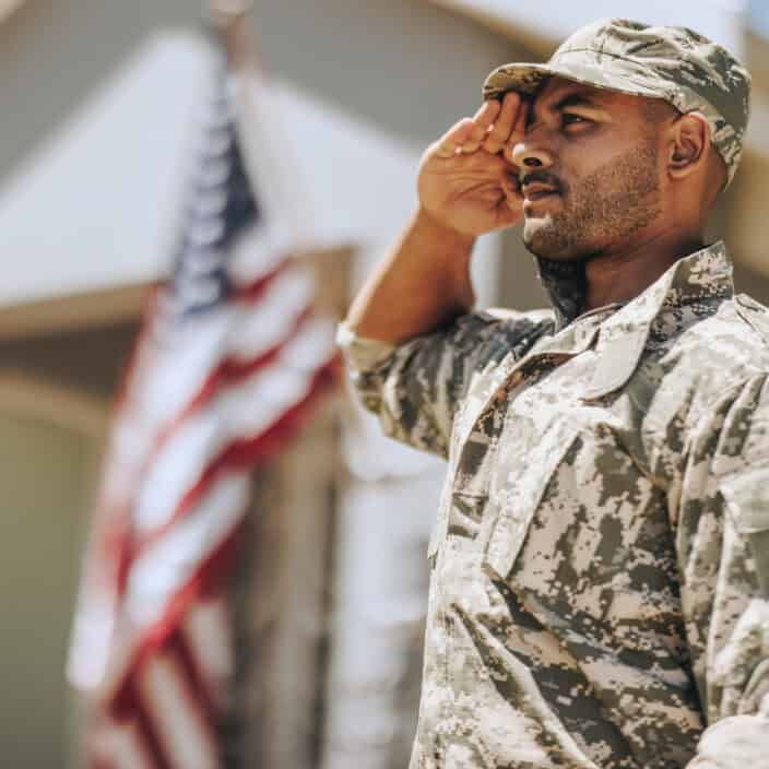 Soldier in camouflage uniform saluting with American flag in background
