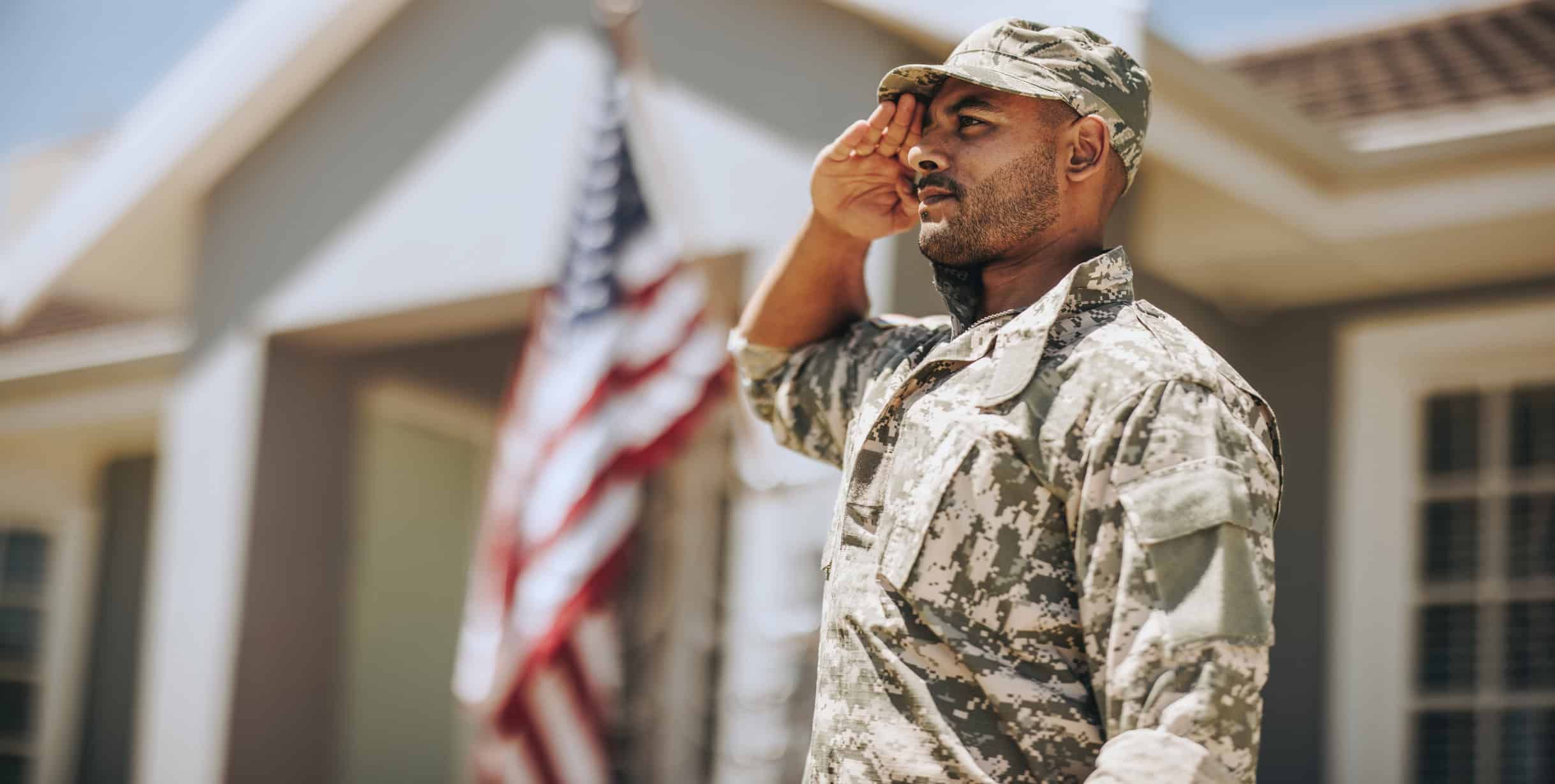 Soldier in camouflage uniform saluting with American flag in background