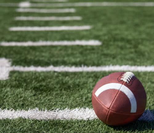 American football on green turf field with white yard line markers