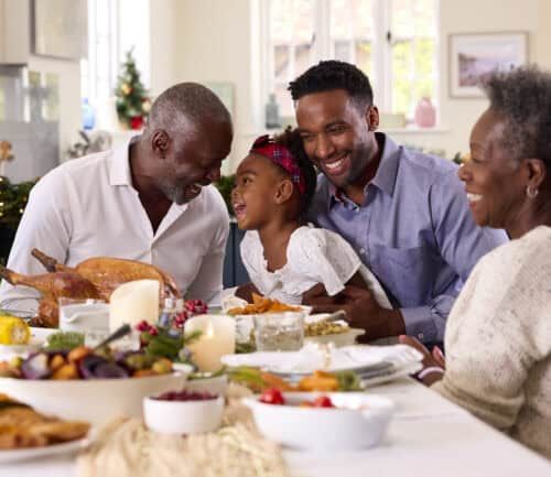 Multigenerational Black family sharing Christmas dinner with grandfather carving turkey at home
