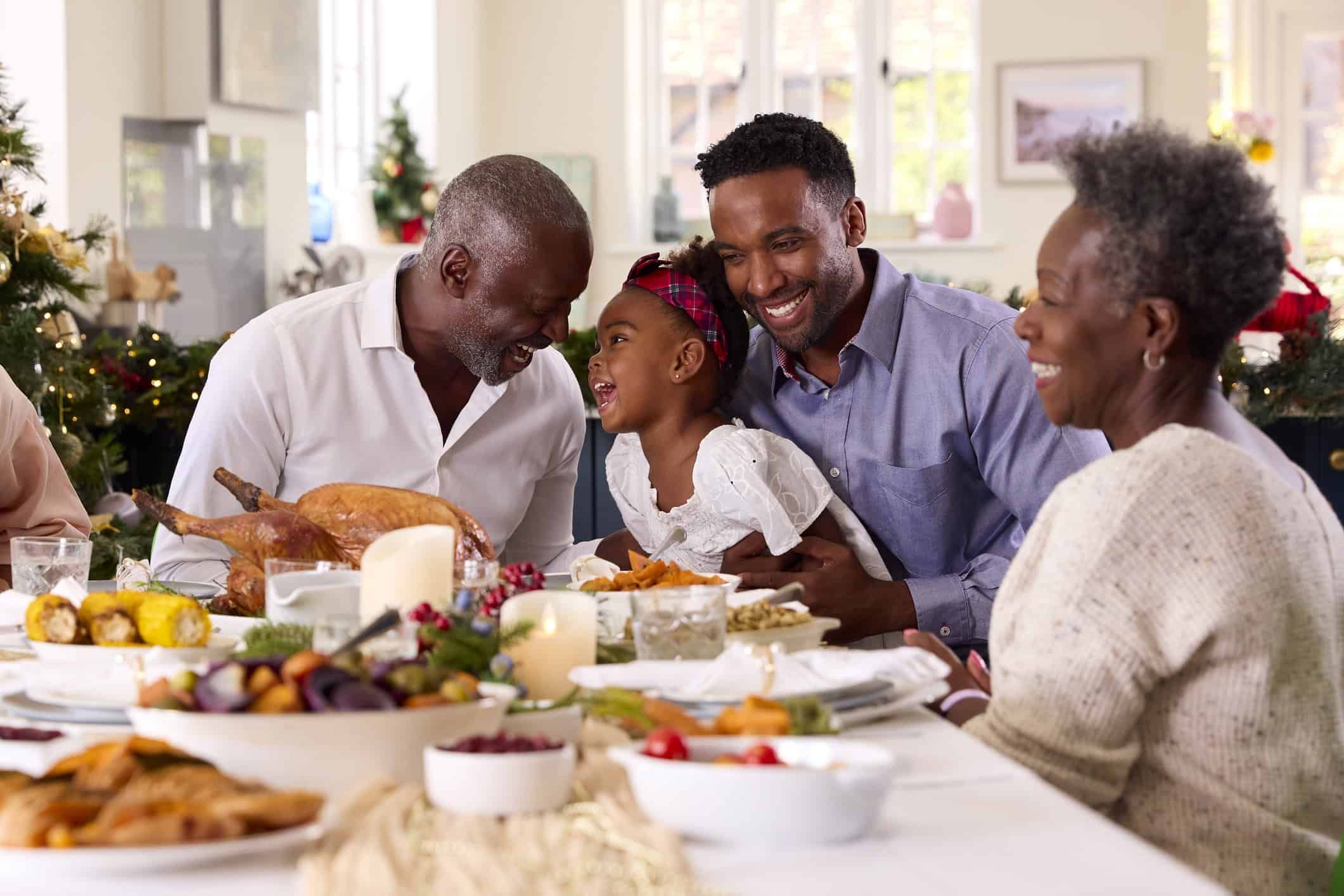 Multigenerational Black family sharing Christmas dinner with grandfather carving turkey at home