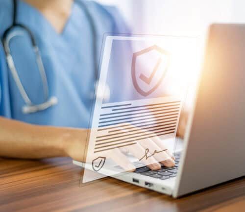 Doctor in scrubs typing on laptop with digital healthcare insurance document overlay