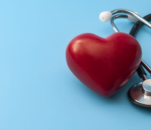 Red heart-shaped object with stethoscope on light blue background for cardiac health concept